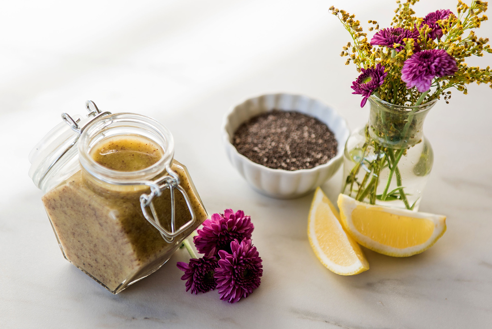 Lemon Poppy Seed Dressing alongside chia seeds, lemon wedges, and flowers on a marble surface.