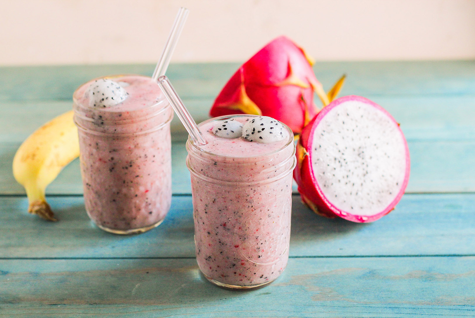 pink dragon fruit smoothie in mason jars next to sliced dragon fruit and banana