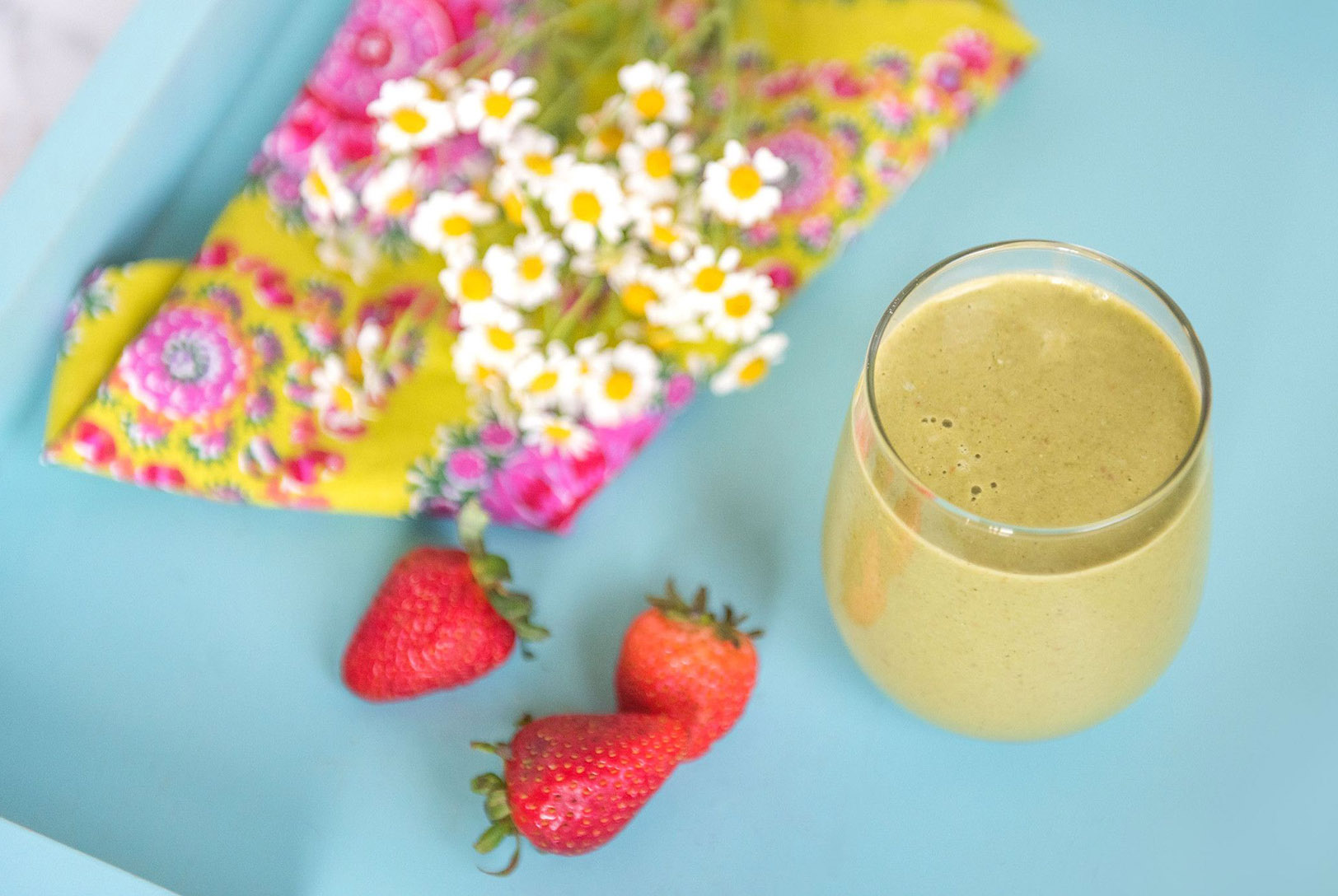 cup of green smoothie next to fresh strawberries and fresh flowers 