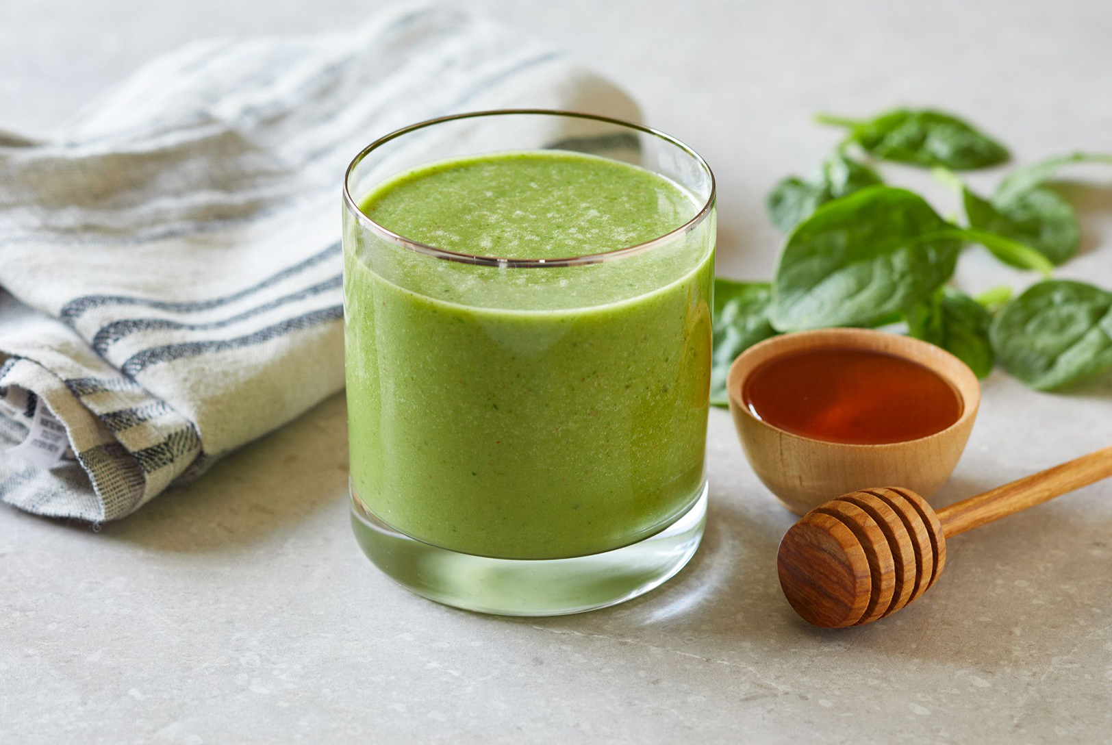 green smoothie in a glass on a kitchen counter next to honey and fresh mint 