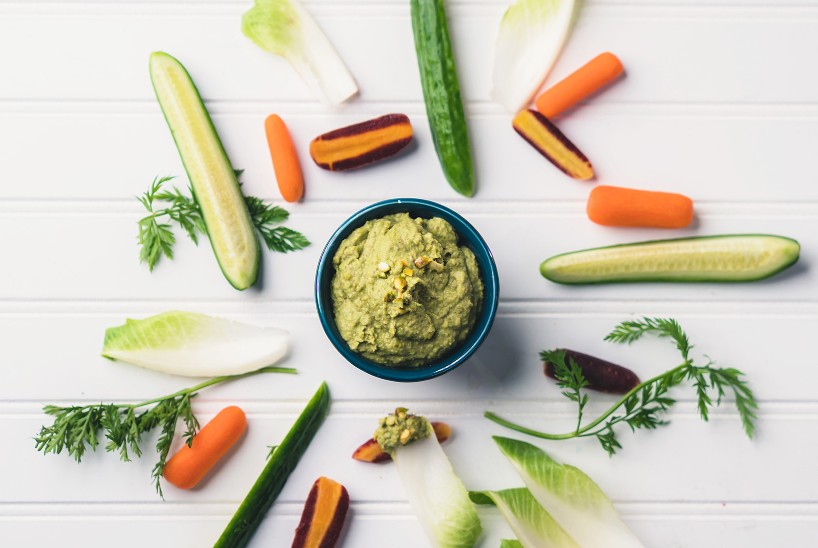 Pistachio herb dip garnished with fresh herbs and whole pistachios surrounded by fresh vegetables and herbs.