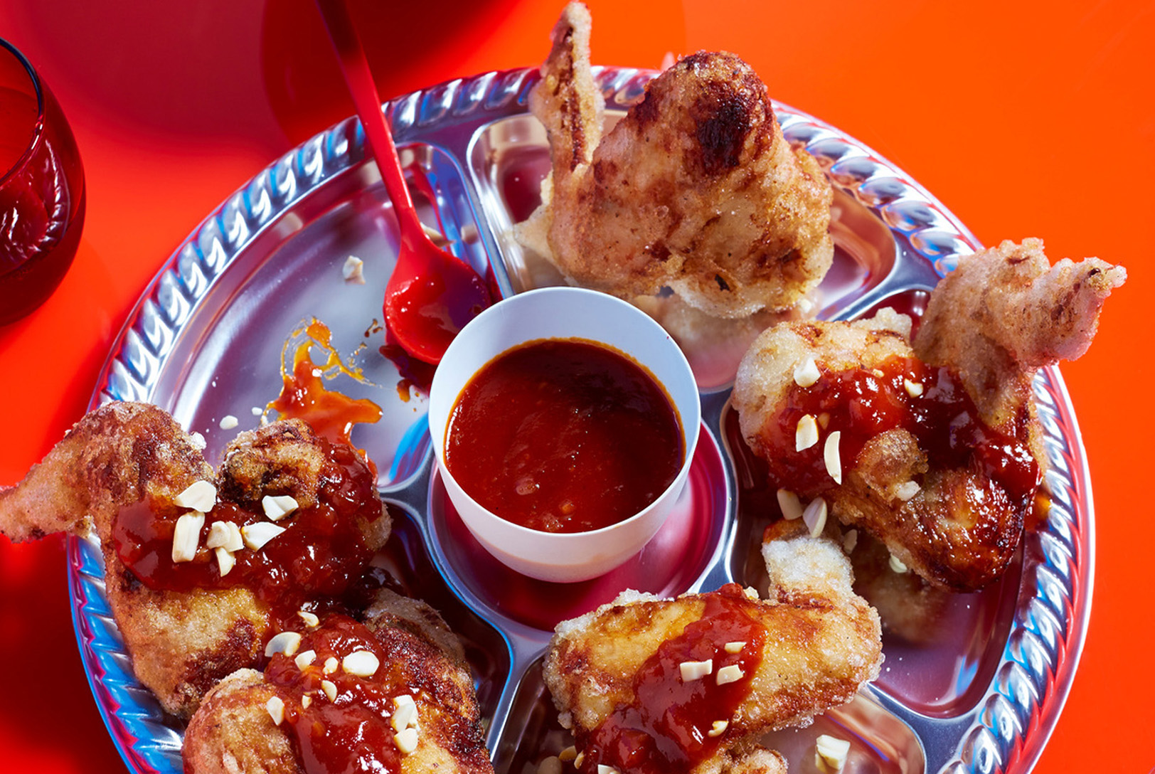Chicken wings drizzled with homemade BBQ sauce and sprinkled with chopped nuts, arranged around a bowl of the same BBQ sauce.