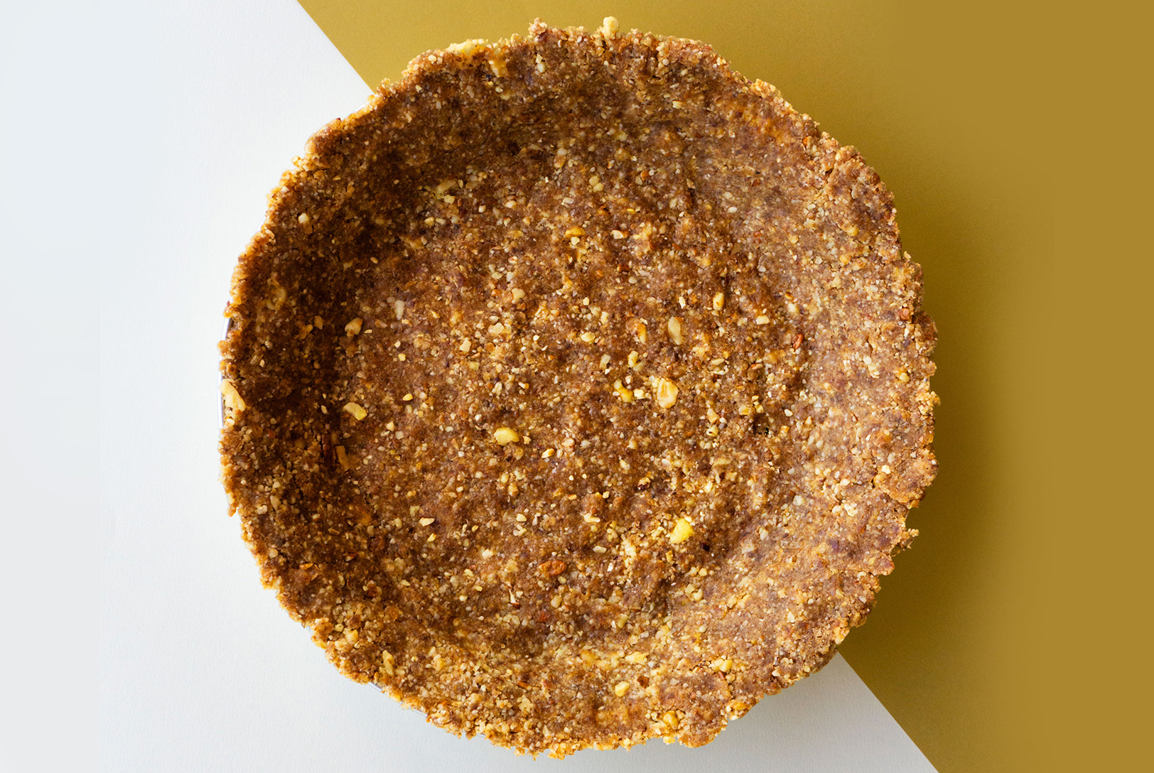 Top-down view of a No-Bake Crust, ready to be filled, set against a diagonally split background of white and warm gold.