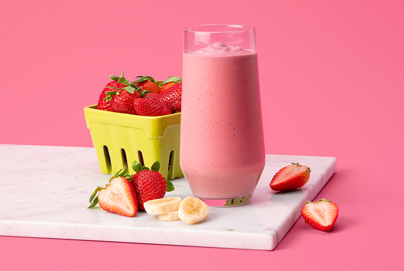 strawberry banana smoothie in a cup next to a pint of fresh strawberries