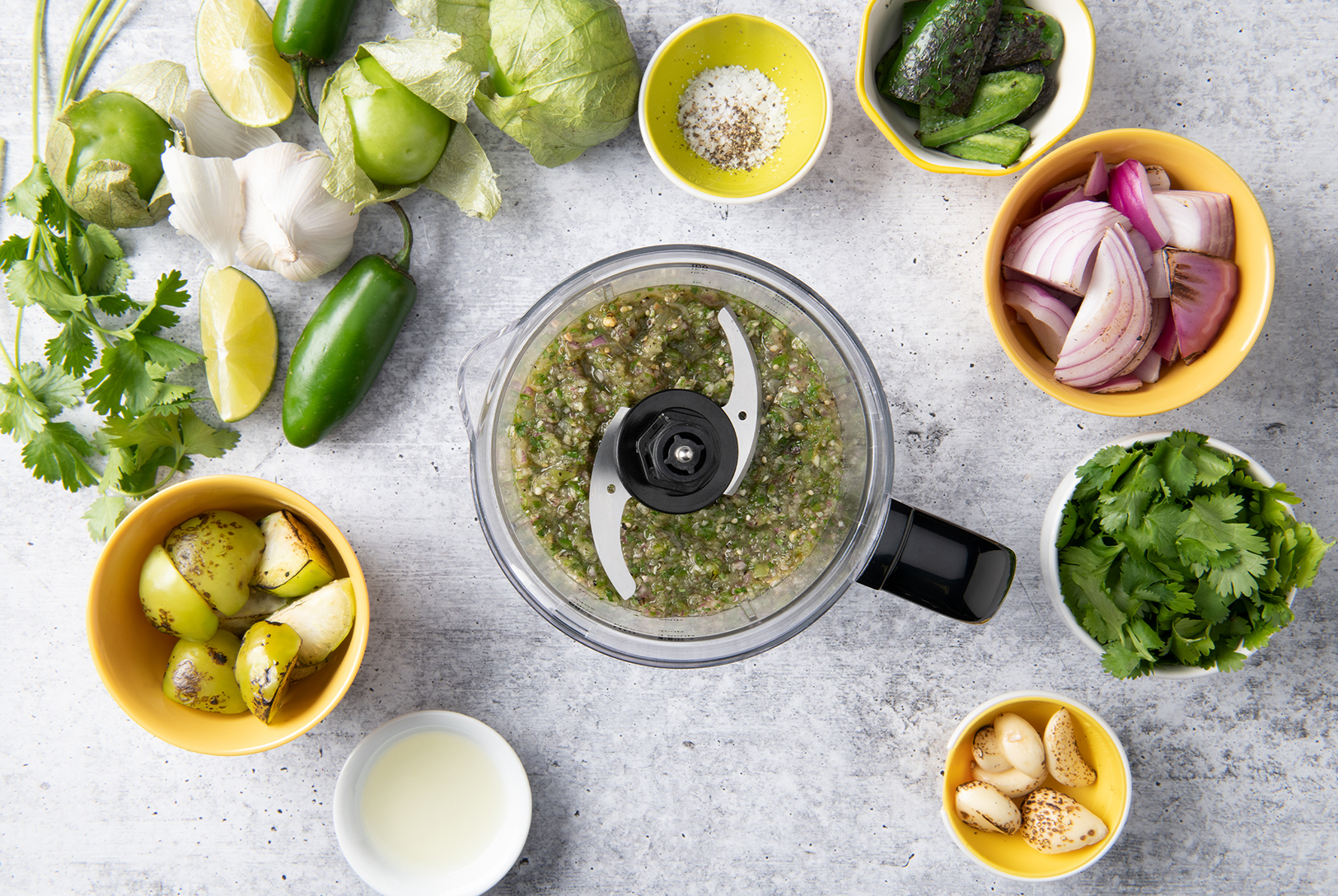 work bowl with salsa verde surrounded lime, jalapeno, garlic, cilantro and tomatillos