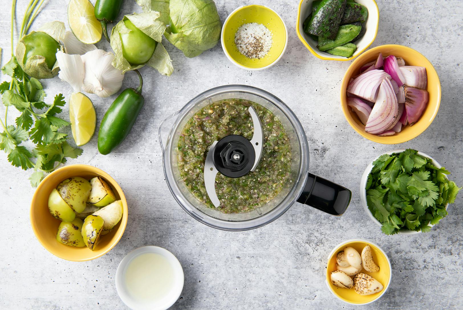 work bowl with salsa verde surrounded lime, jalapeno, garlic, cilantro and tomatillos