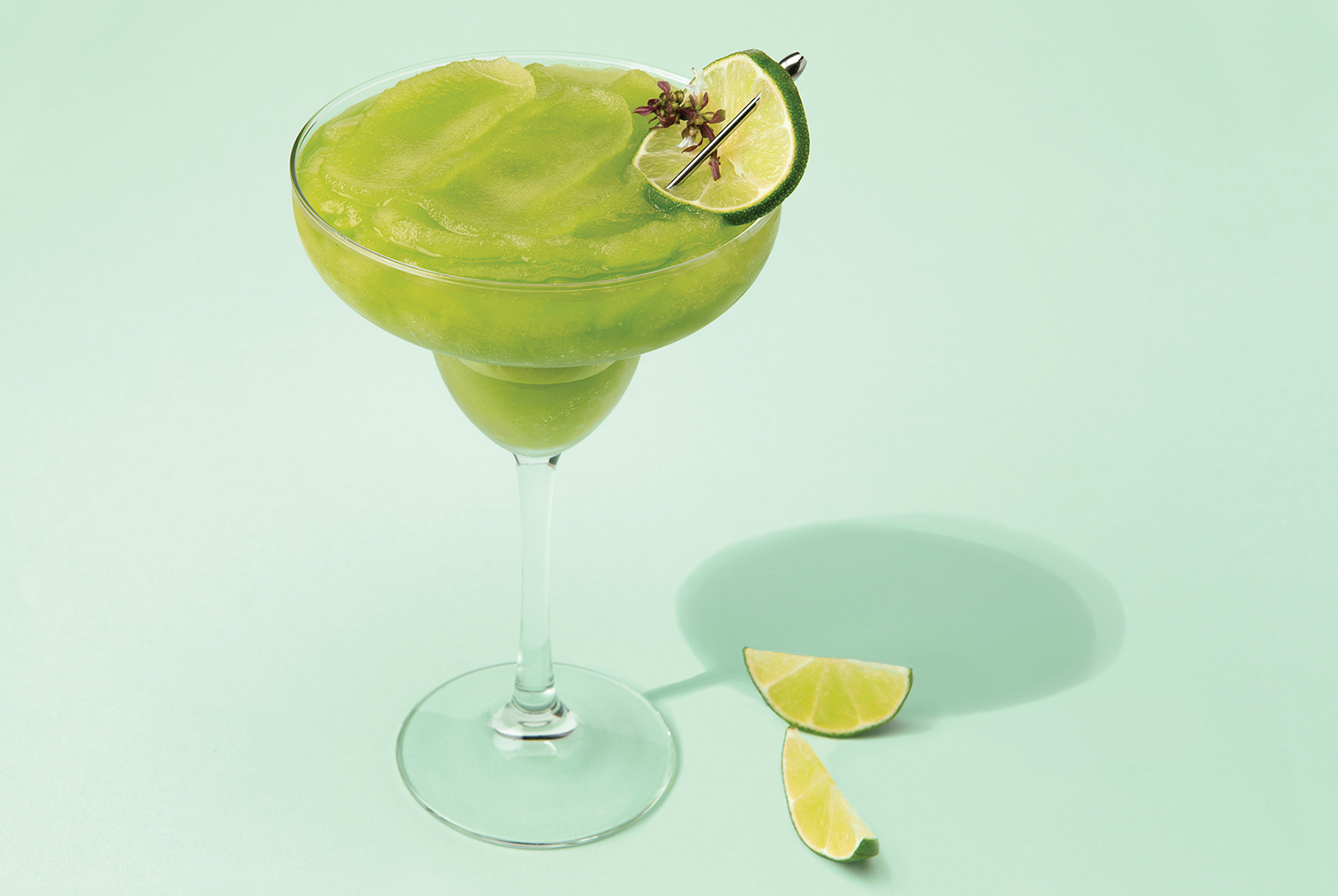 glass of lemon lime margarita with basil and lime wedges