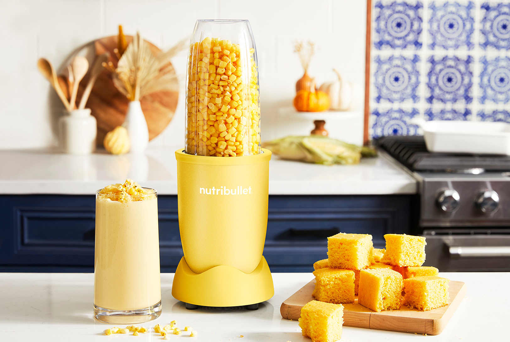 cup of blended corn next to a yellow nutribullet blender along with a plate of cornbread on a kitchen counter