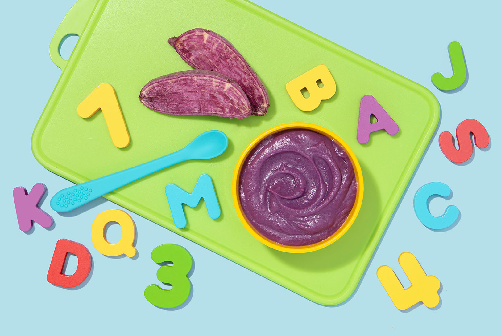 Kidney bean, sweet potato, and cinnamon puree on a green cutting board surrounded by baby toys