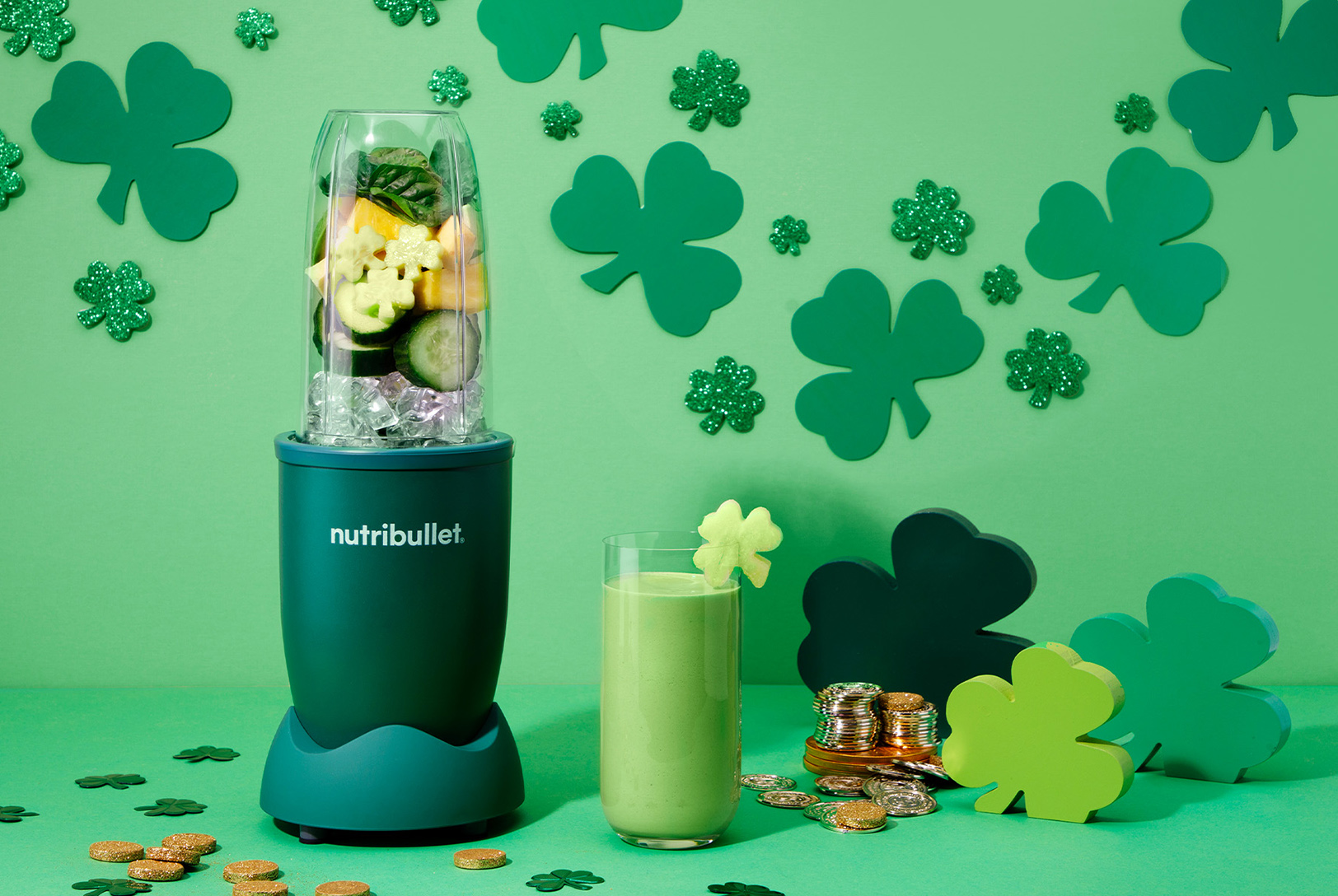 A nutribullet blender with green and yellow ingredients next to a green smoothie garnished with a shamrock, surrounded by St. Patrick's Day decorations.