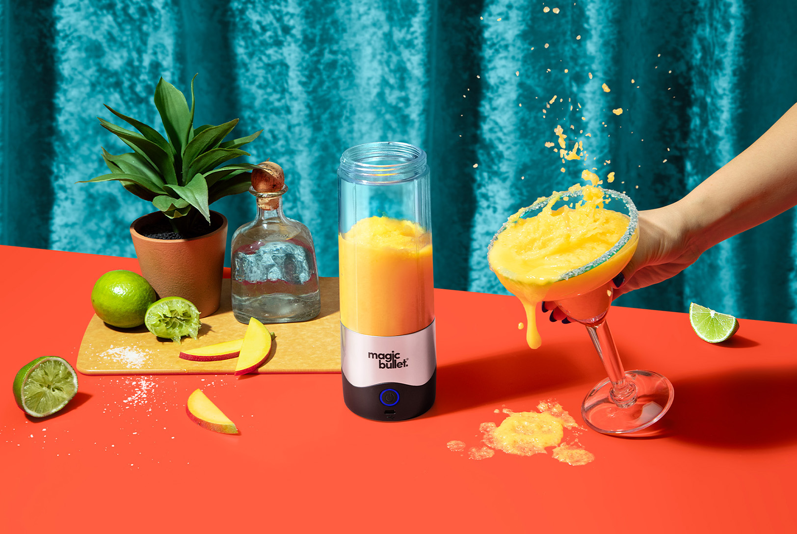 frozen yellow mango margarita in magic bullet Portable Blender surrounded by cocktail garnish