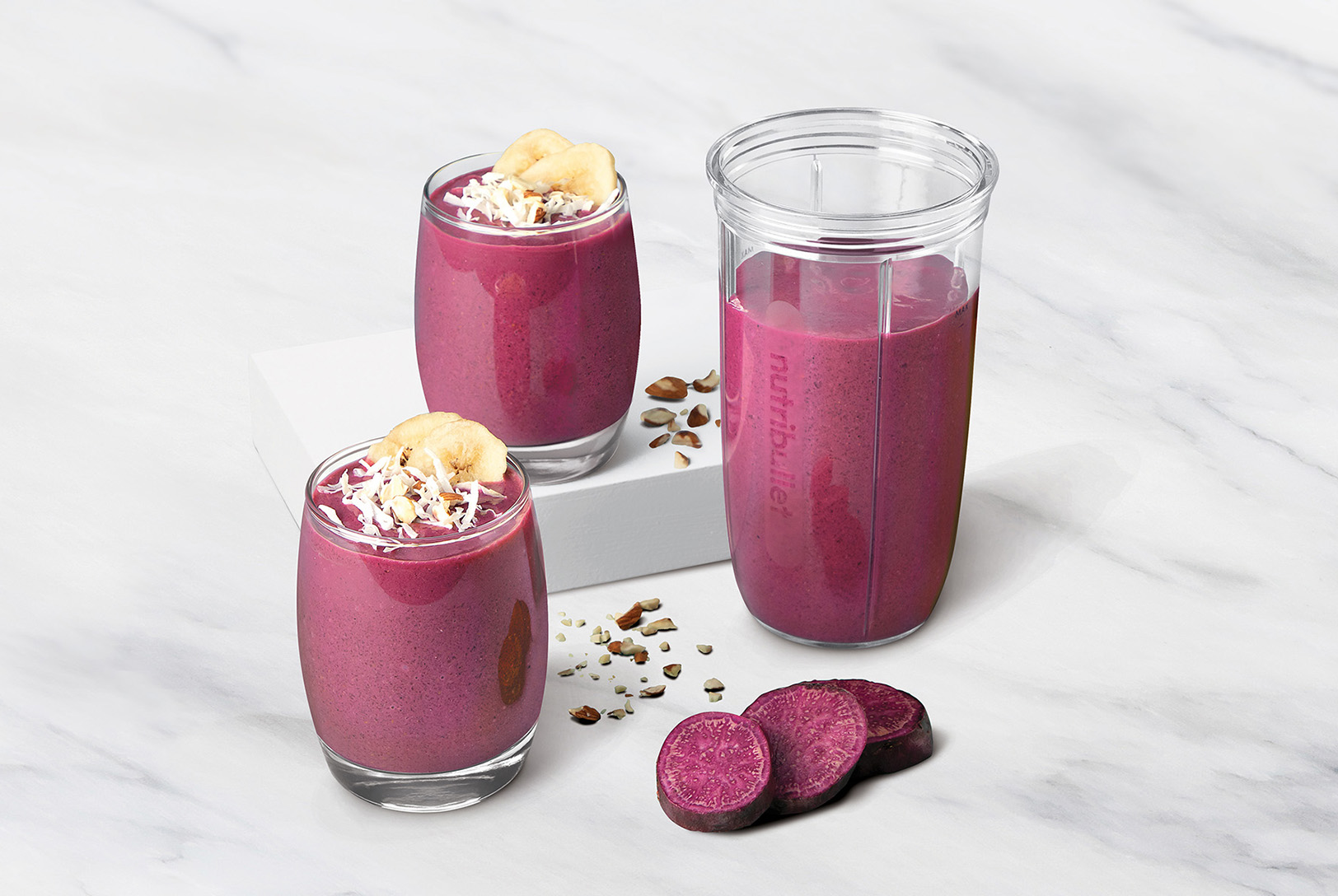 Purple sweet potato pie smoothies topped with sliced banana and coconut on turquoise background