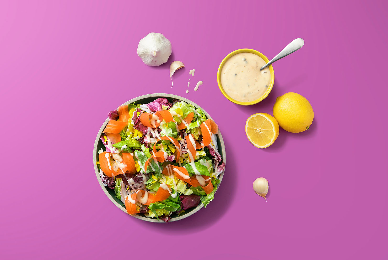 Green salad with shaved carrots and beets topped with Vegan Caesar Dressing on purple background