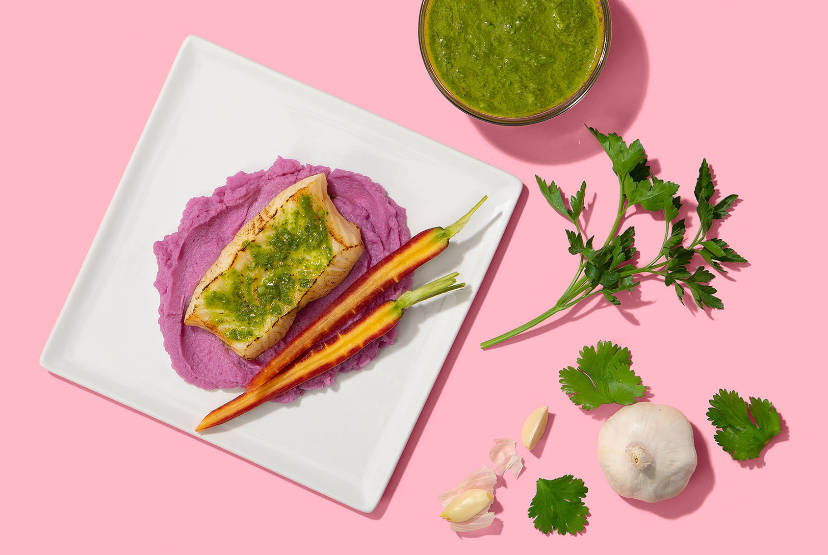 salmon and roasted carrots topped with chimichurri on white plate with pink background