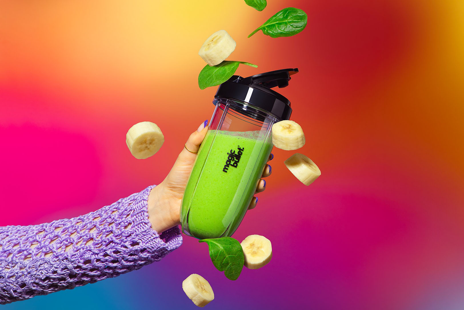 Blended green smoothie in to-go cup surrounded by sliced bananas and spinach