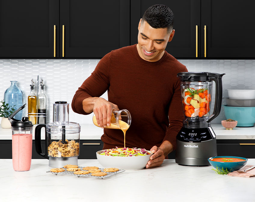 Man pouring salad dressing from a cup to a salad sitting next to the nutribullet Triple Prep