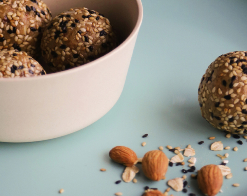 Creme bowl filled with brown seeded balls next to a ball, seeds, oats and nuts on blue surface.
