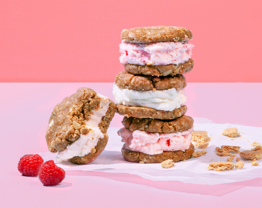 Four Ice cream sandwhiches, with raspberries against a pink background