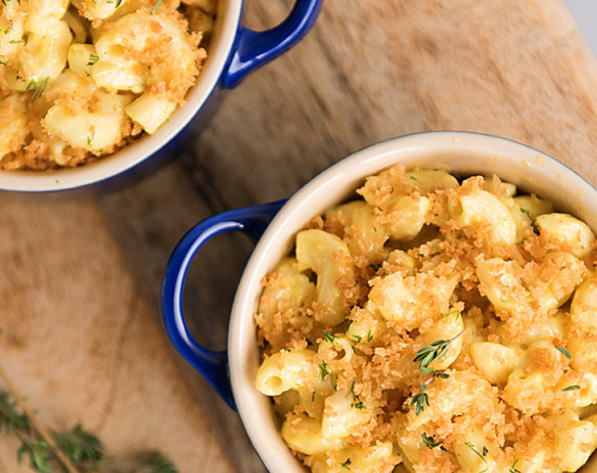 Two blue bowls of mac and cheese topped with breadcrumbs and herbs on wooden surface.