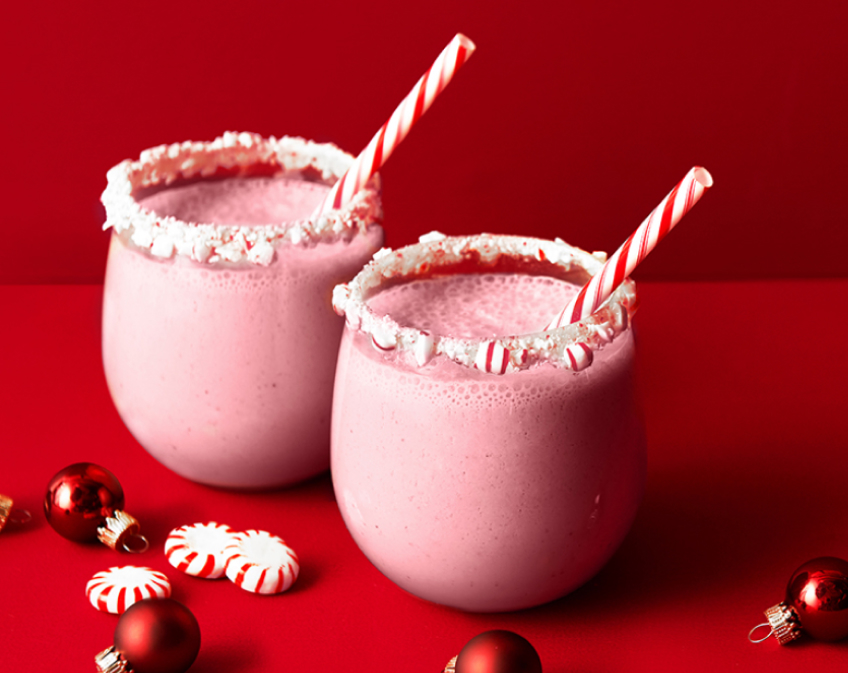 Two pink drinks with candy cane rims and red and white striped straws on red background.