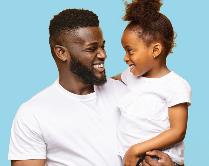Smiling father in white shirt holding smiling little girl in white shirt on blue background.