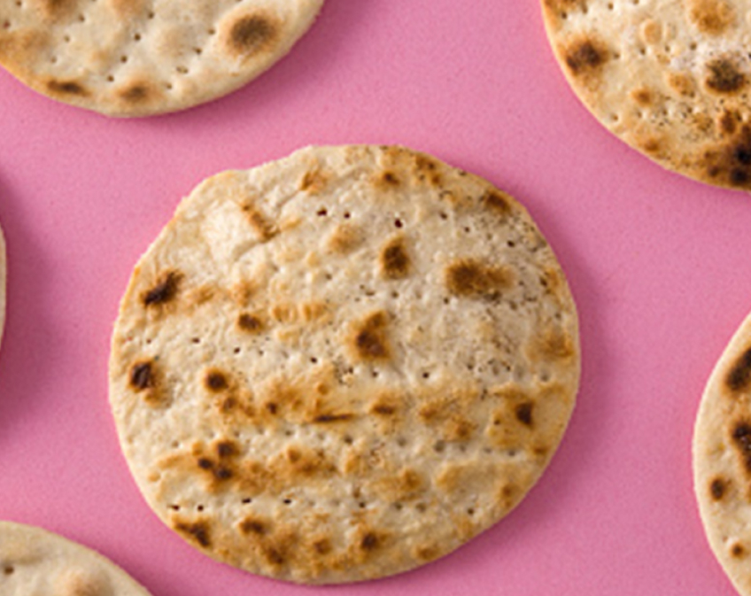 Cooked circular flat bread on a pink background.