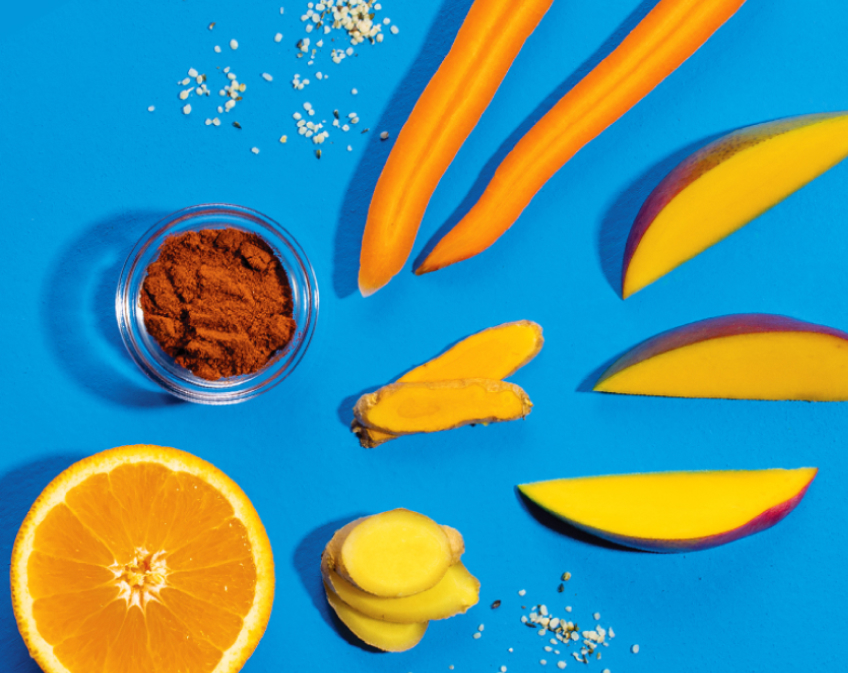 Sliced fruit, vegetables, a dish of spice, and seeds on a blue surface.