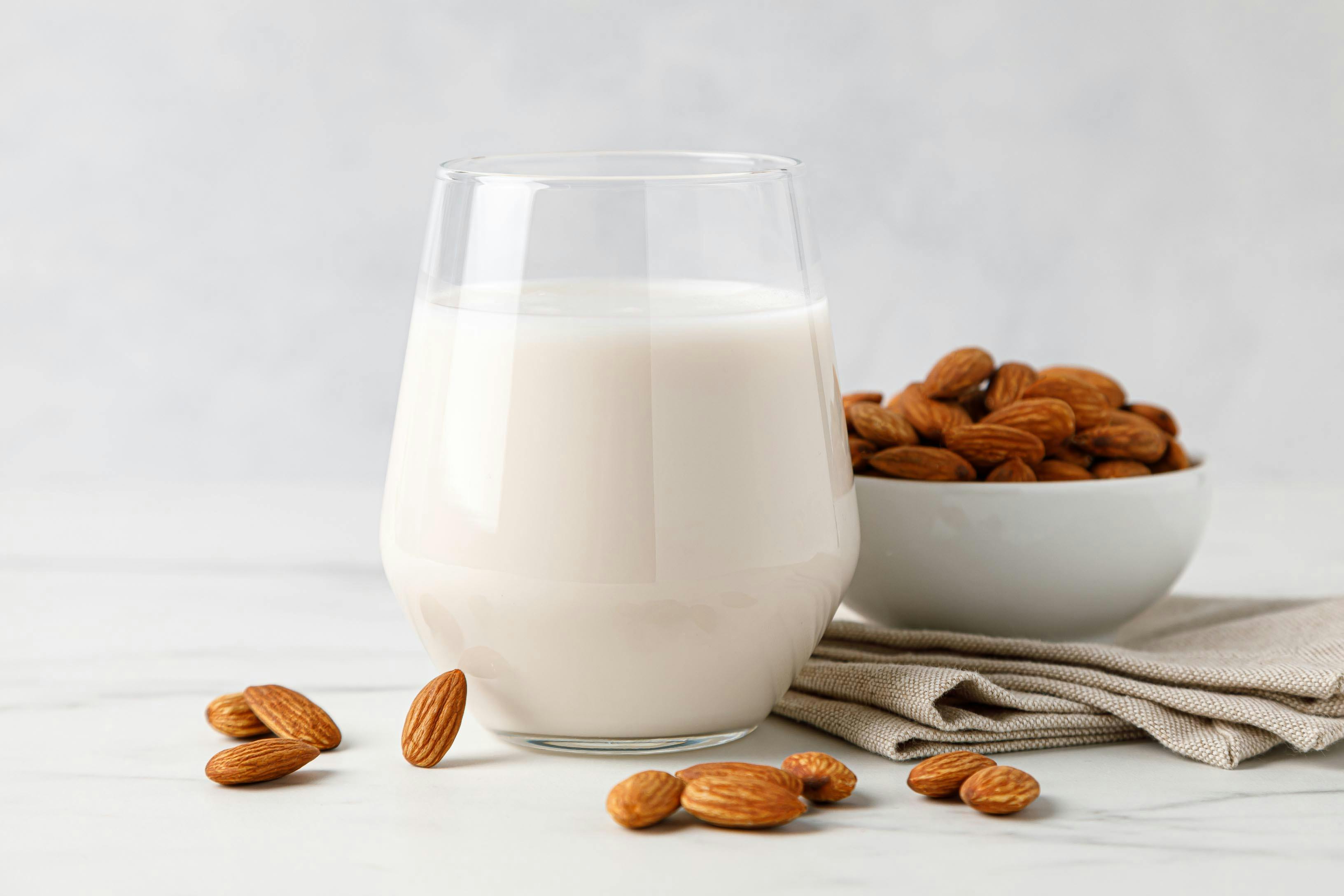 glass of homemade almond milk next to a bowl of raw almonds on a napkin