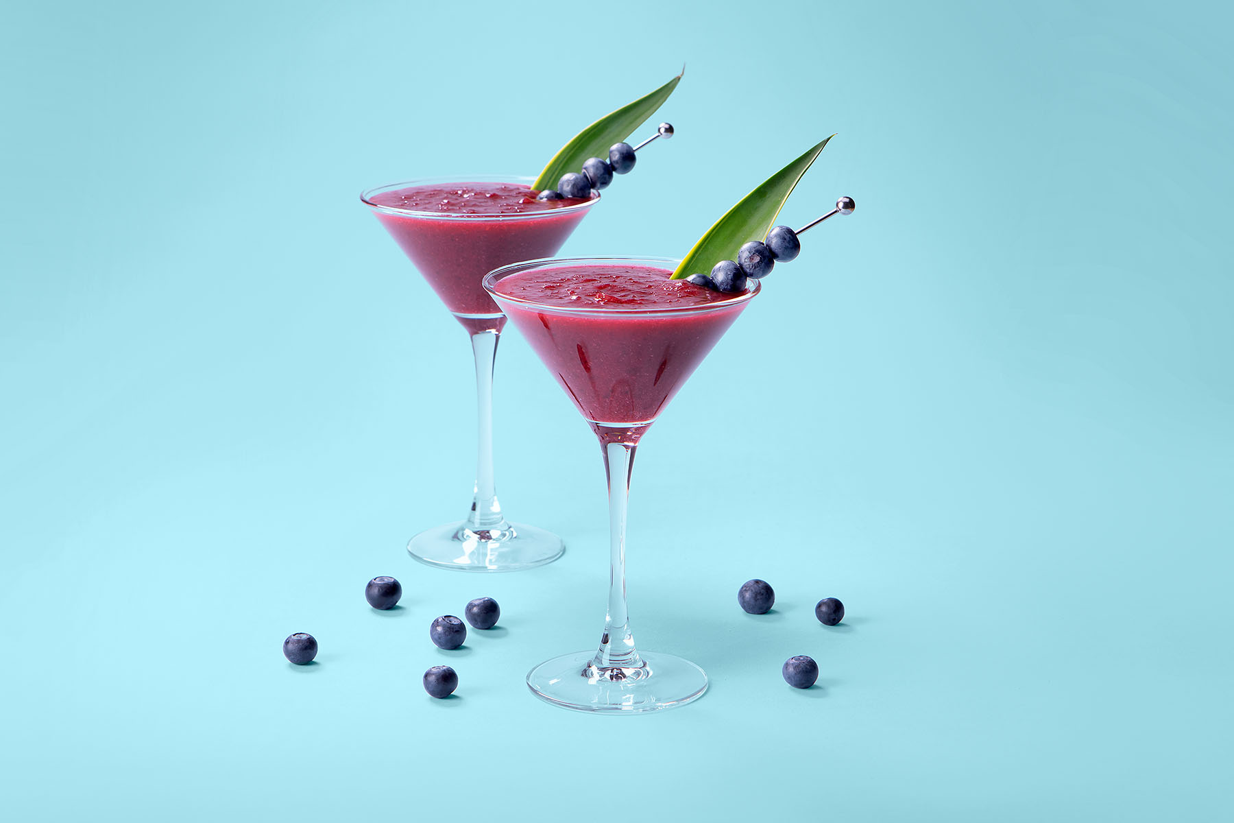 Berry cocktails in martini glasses with blueberry skewers for garnish with blue background