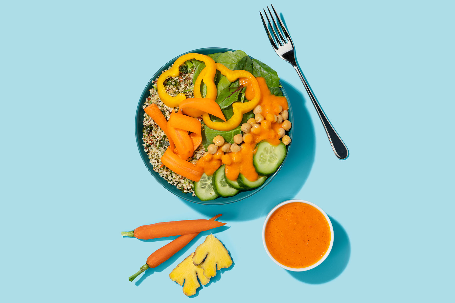 Quinoa salad with spinach, bell pepper, and cucumber topped with Carrot Ginger Miso Dressing with blue background