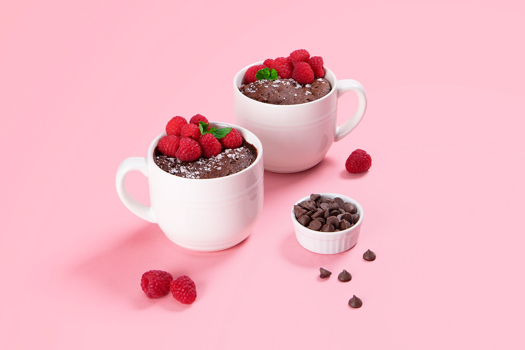 Chocolate Mug Cake in white mugs topped with fresh raspberries on pink background