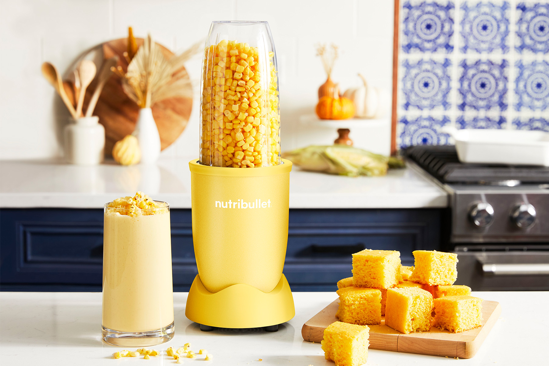 cup of blended corn next to a yellow nutribullet blender along with a plate of cornbread on a kitchen counter