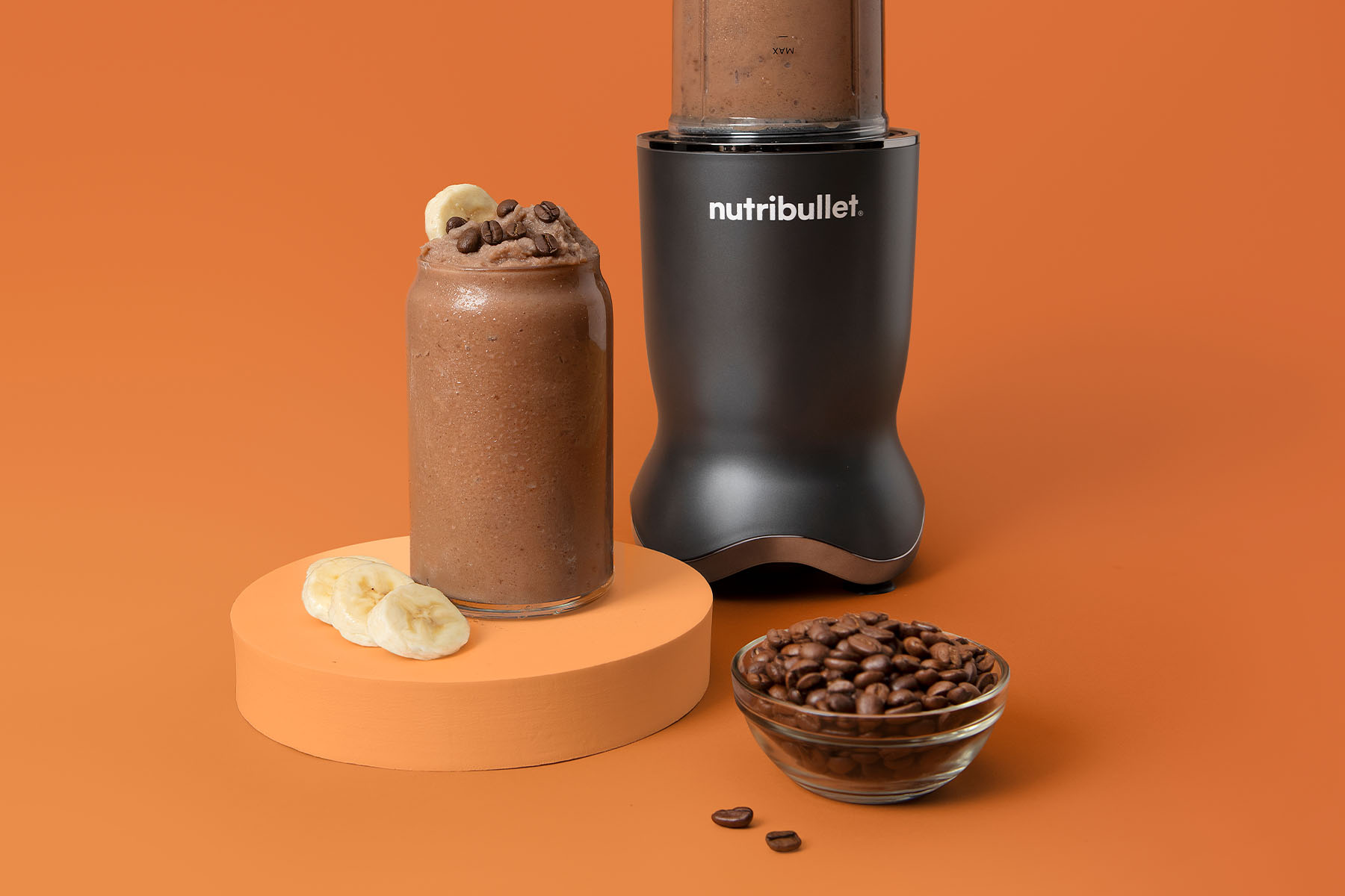 Creamy coffee smoothie in a nutribullet Ultra garnished with banana slices and chocolate chips on orange background