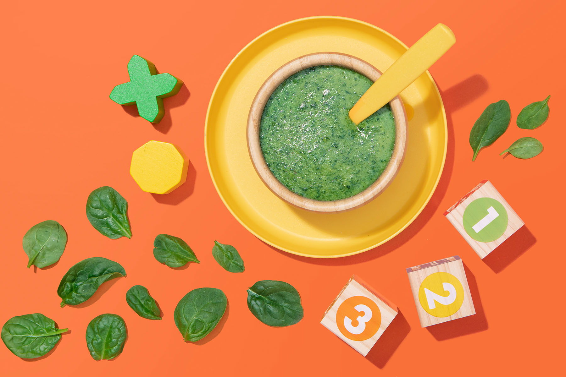 A bowl of blended spinach and potato with spinach leaves and number blocks outside