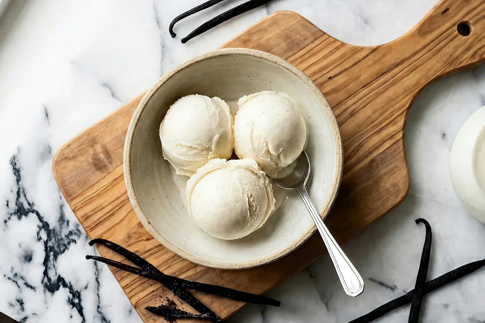 scoops of French vanilla ice cream on a wooden cutting board surrounded by vanilla bean