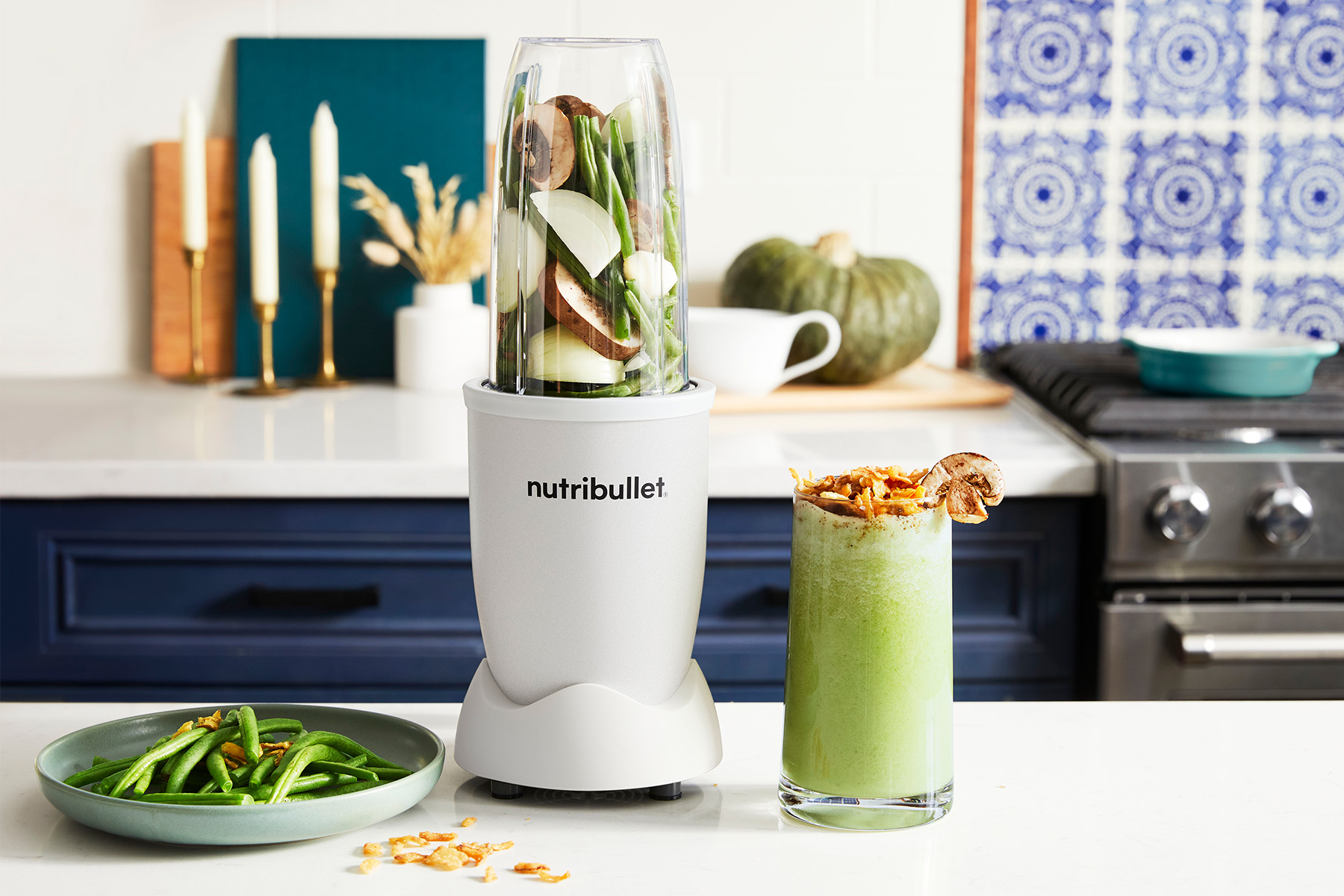 Glass of blended green beans next to a white nutribullet blender and a plate of green beans on a kitchen counter
