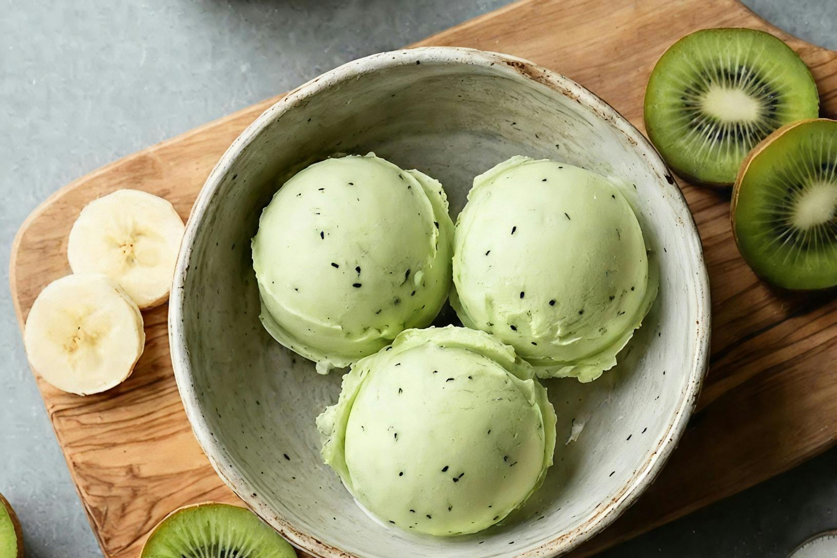 scoops of kibana ice cream in a bowl next to fresh slices of banana and kiwi