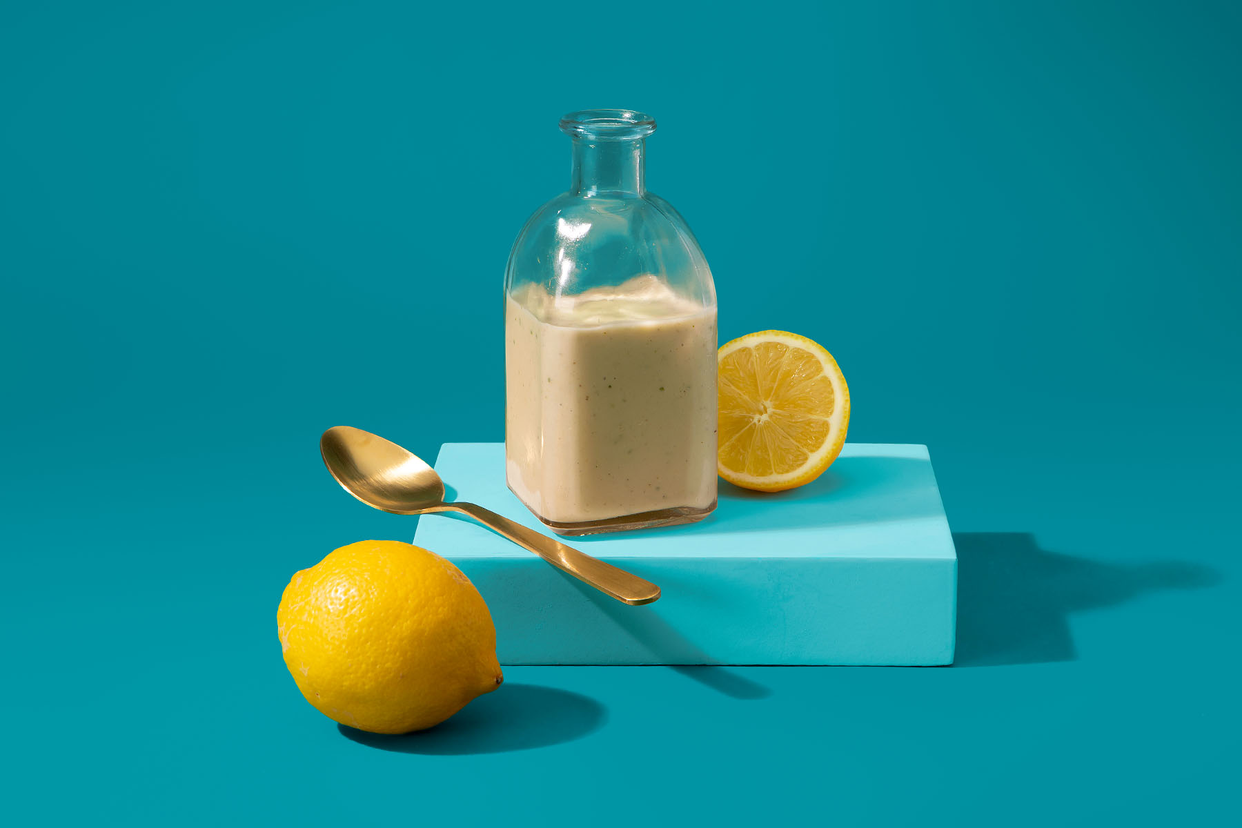 Lemon Tahini Dressing in a jar alongside fresh lemon with blue background 
