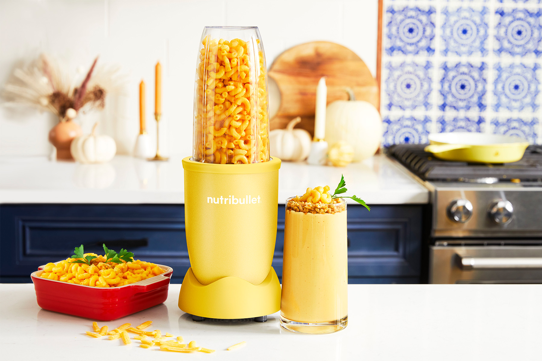 Mac and Cheese in a tray next to a yellow nutribullet blender filled with macaroni next to a blended glass of mac and cheese