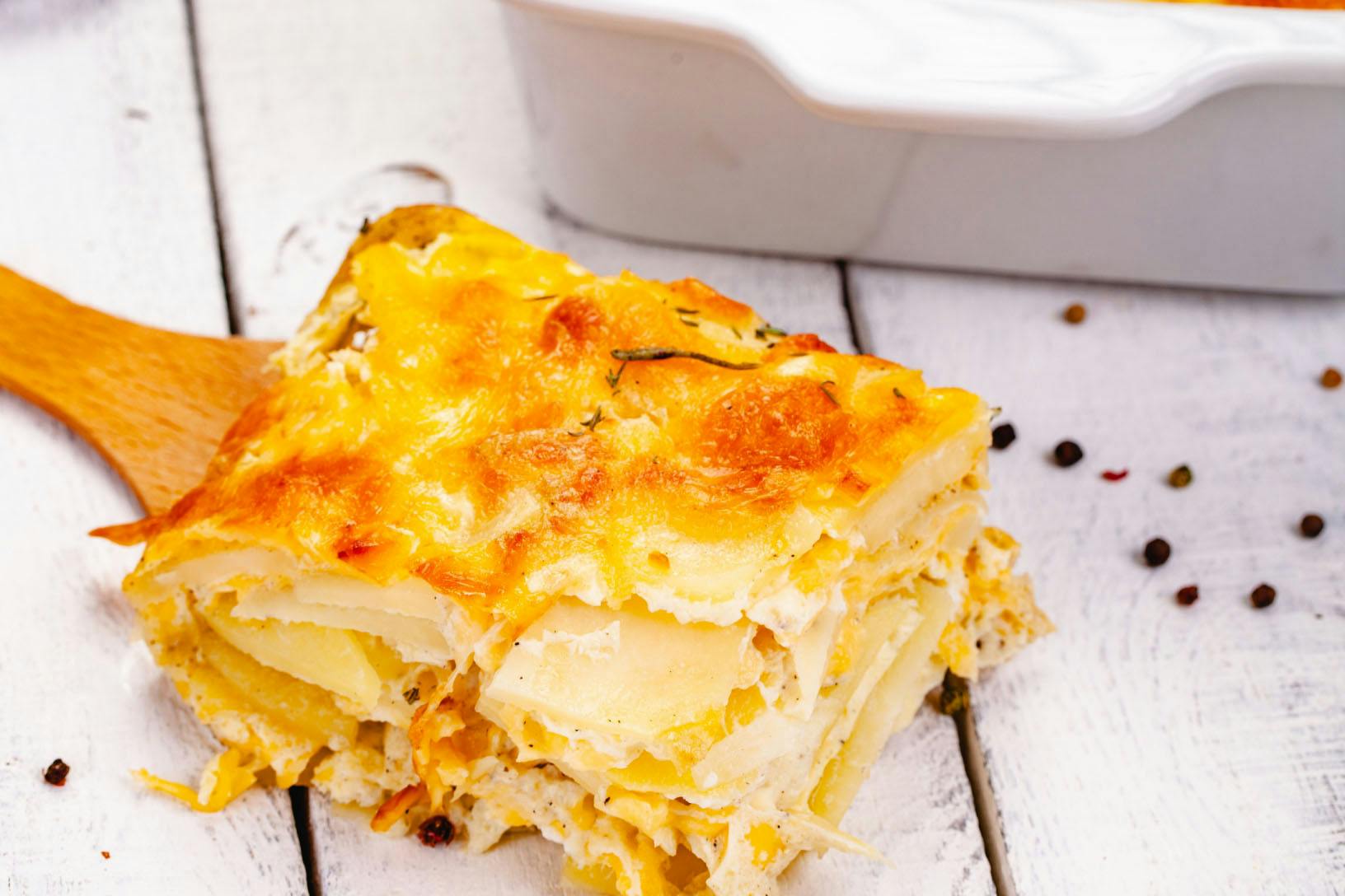 A slice of homemade potatoes au gratin fresh out of the oven on a wooden spatula.