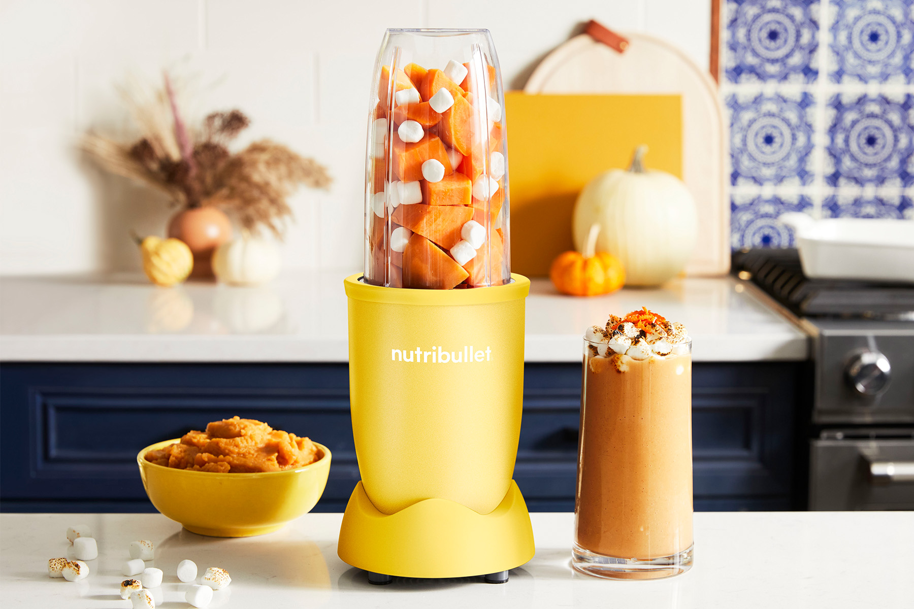 blended sweet potato smoothie with marshmallows next to a yellow nutribullet blender and a bowl of pureed sweet potatoes on a kitchen counter
