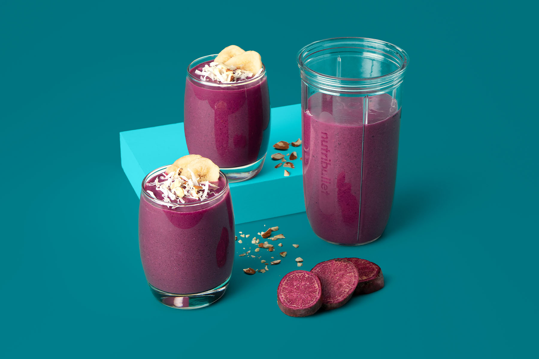 Purple sweet potato pie smoothies topped with sliced banana and coconut on turquoise background
