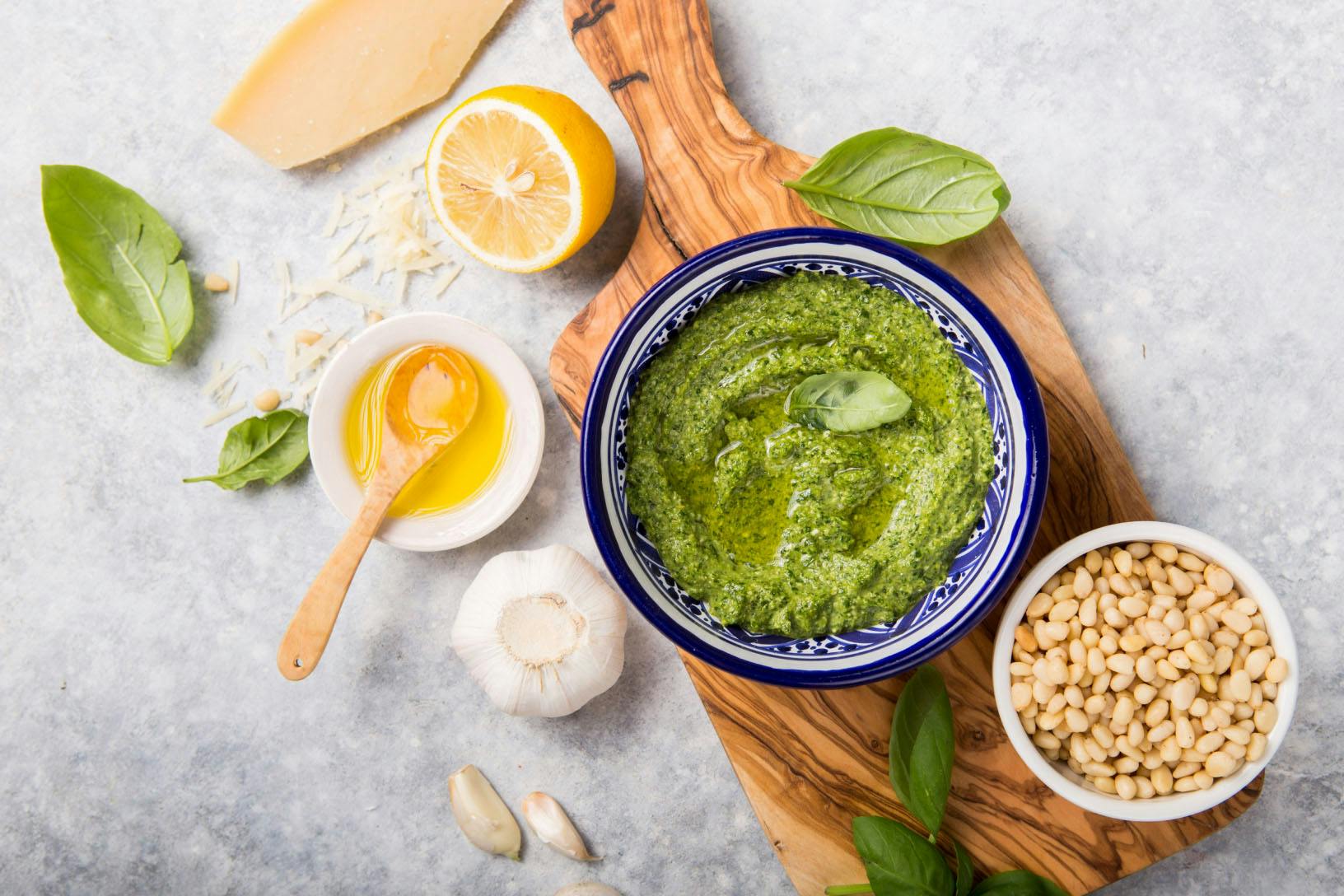 Vegan Scallion and Cashew Pesto a bowl of homemade pesto surrounded by its ingredients, including fresh lemon, basil, pine nuts, and garlic
