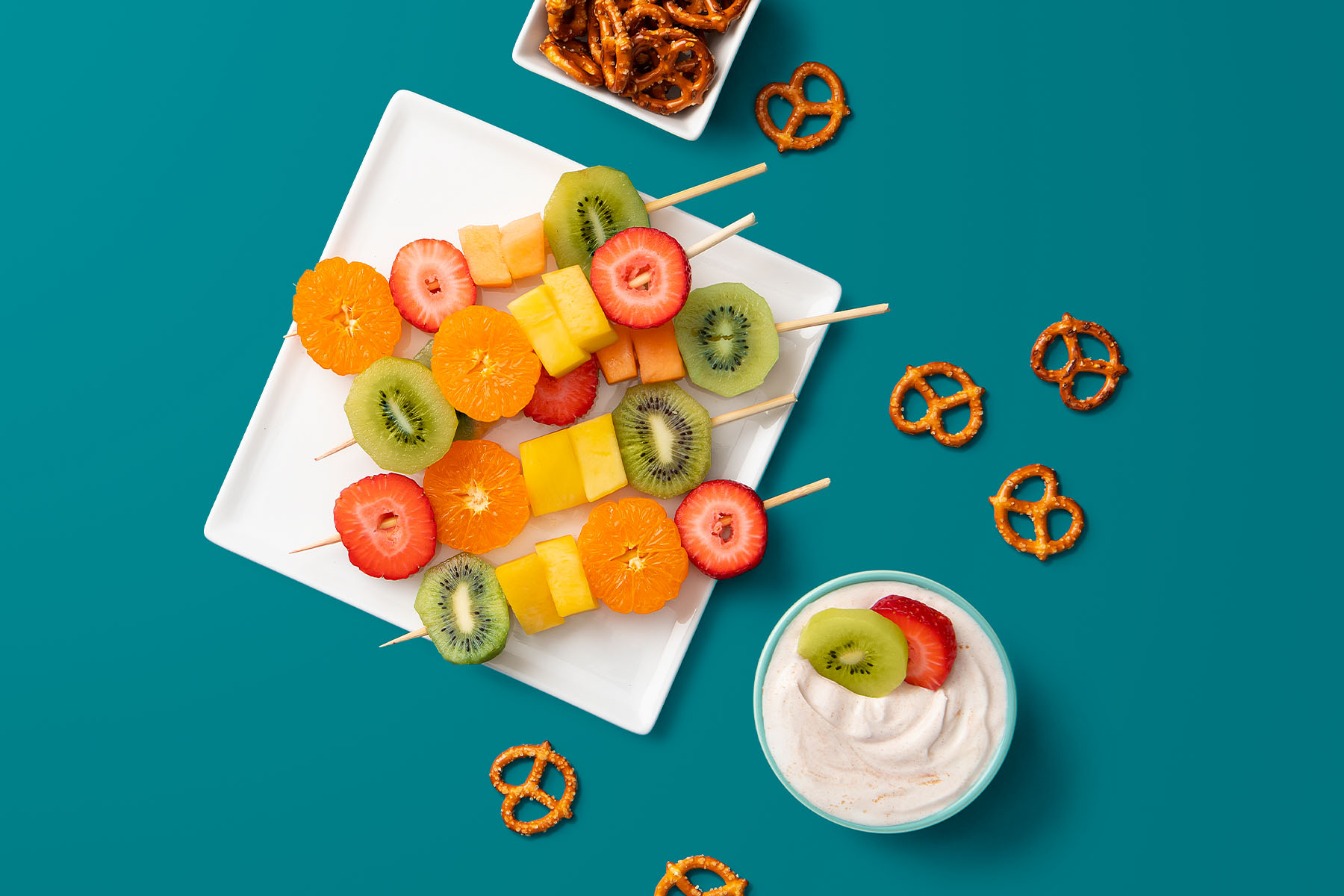 plated fruit skewers on a white plate and pretzels with homemade yogurt dip