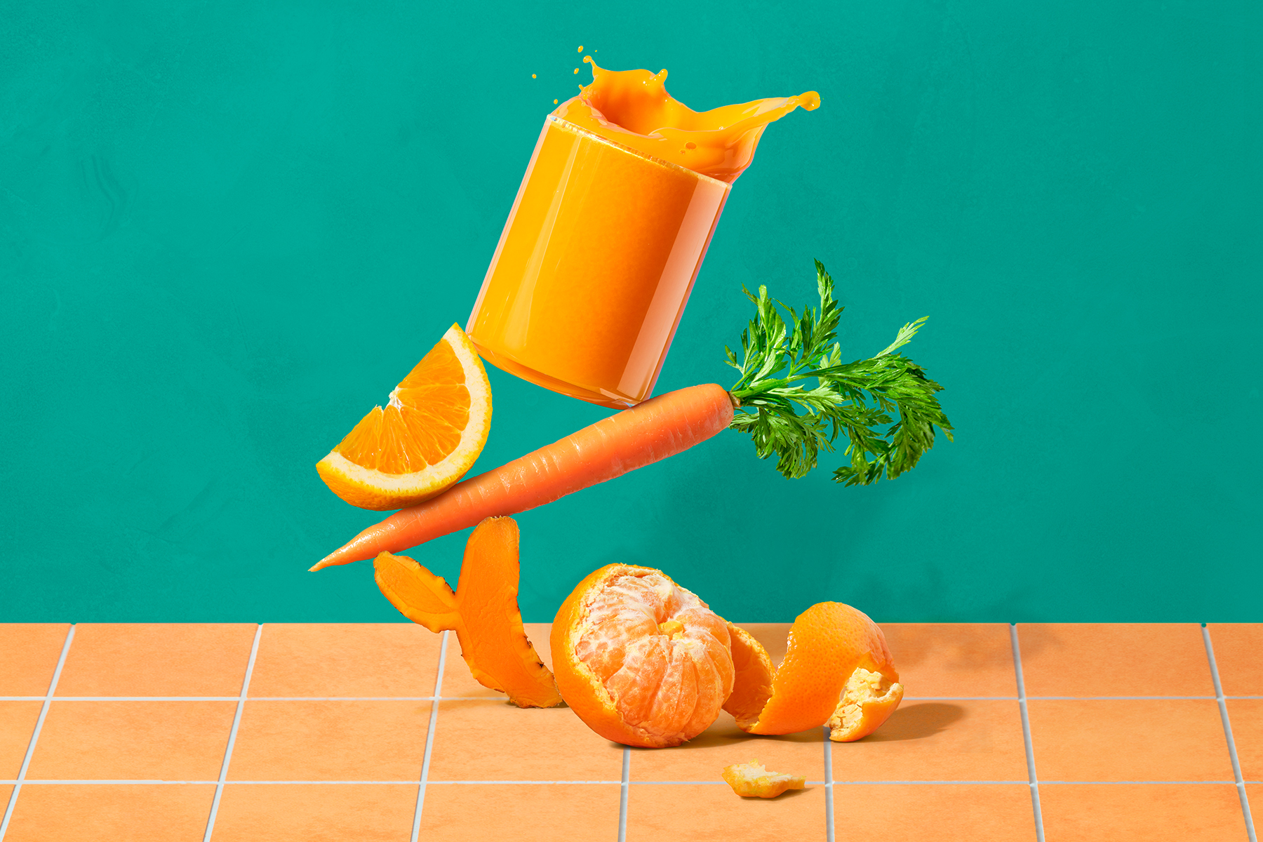 Glass of carrot, orange and turmeric juice sitting on top of those ingredients on an orange counter in front of a green background