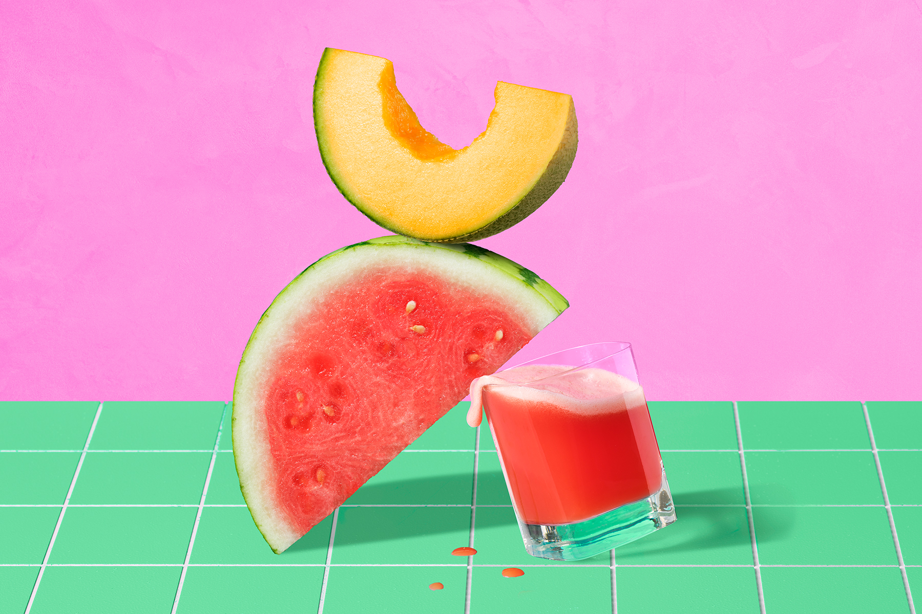 glass of watermelon cantaloupe juice sitting on a green counter with watermelon and cantaloupe slices stacked on top in front of a pink background