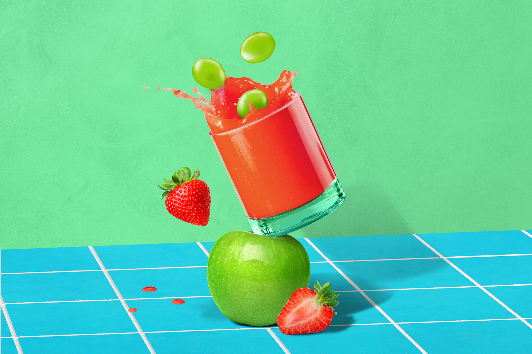 glass of red fruit juice propped on top of a green apple splashing with green grapes, strawberries and green apple on a blue counter with green background