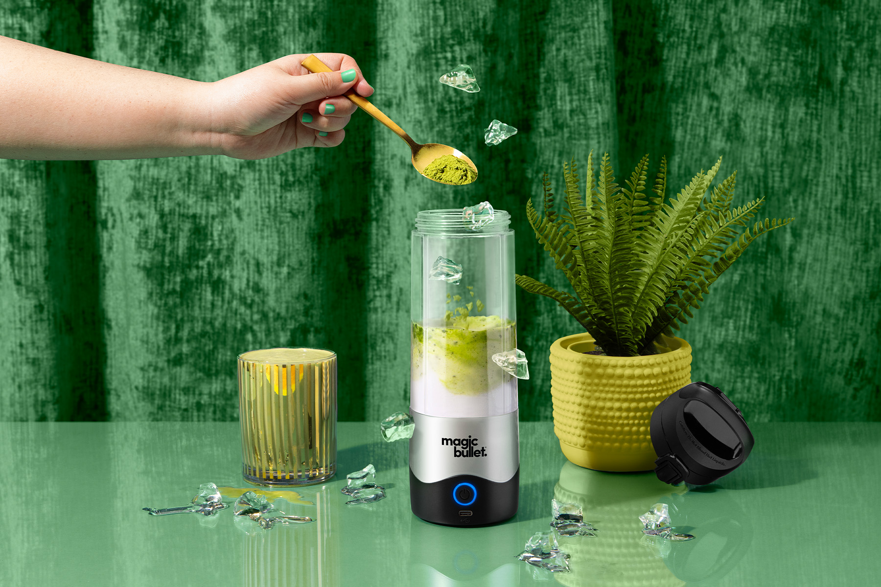 green matcha latte in magic bullet Portable Blender surrounded by ice and decor