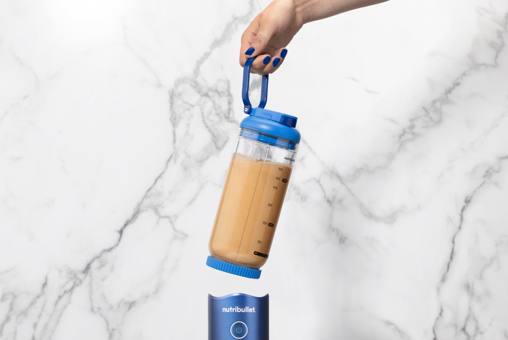 chocolate smoothie in blue portable blender with hand detaching it from motor base and carrying away