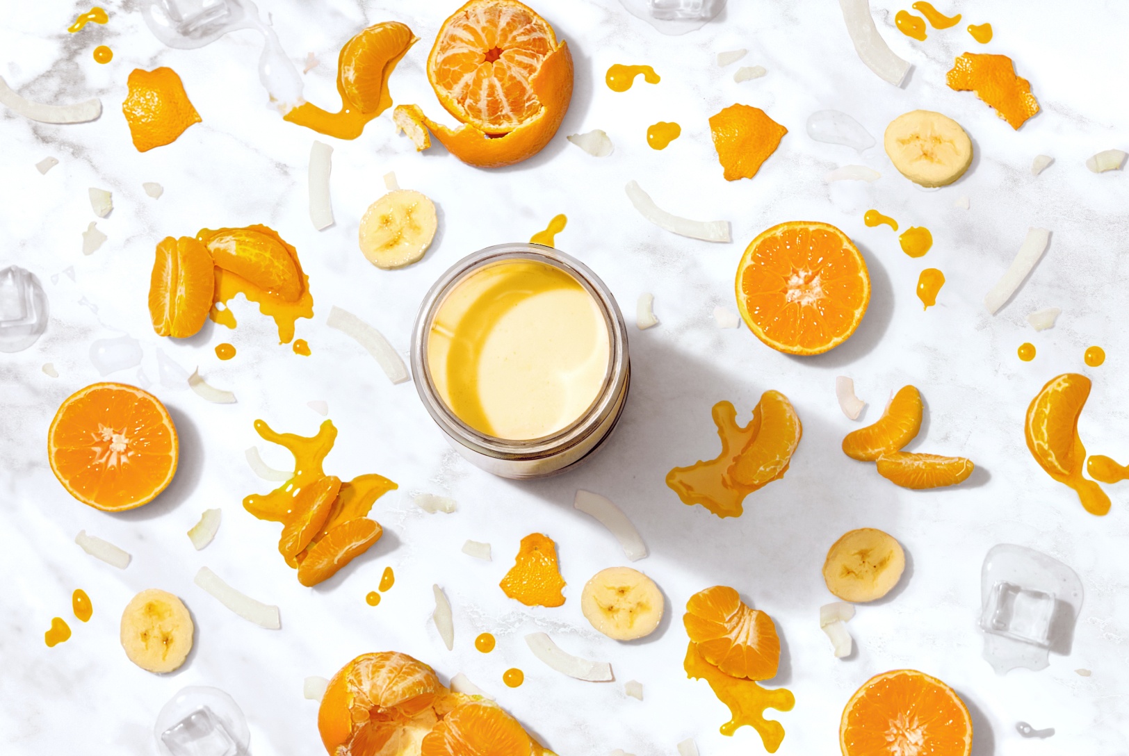 A bird's eye view of a light orange smoothie decorated with orange slices, banana slices, and coconut strips. 